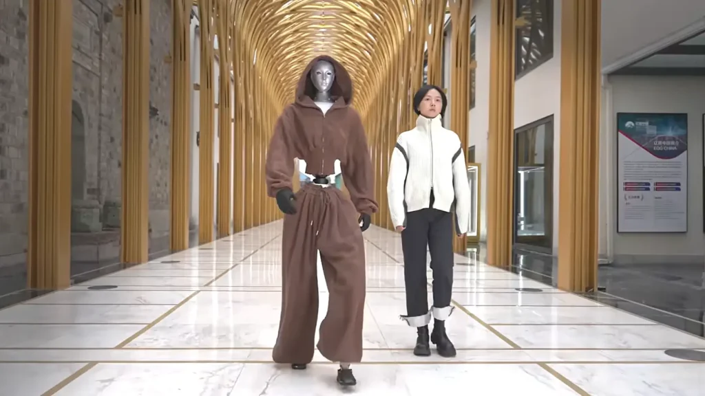 Robot UNitree H2 avec une veste marron marche à coté d'une femme